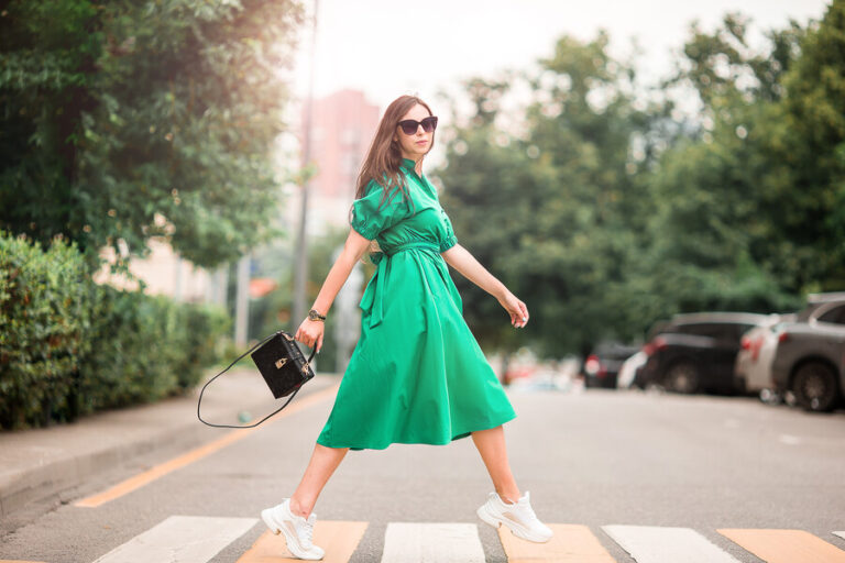 Cette femme qui marche dans la rue avec une robe verte et un sac à main noir a choisi des tennis blanches