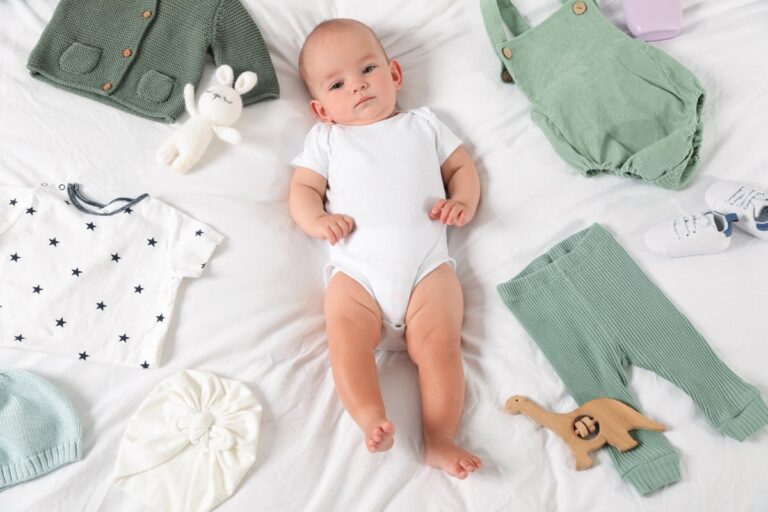 Un bébé allongé sur le lit et entouré par des petits vêtements