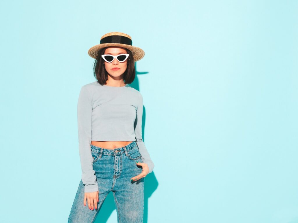 Une jolie femme portant un chapeau, une lunette, un crop top et un jean bleu