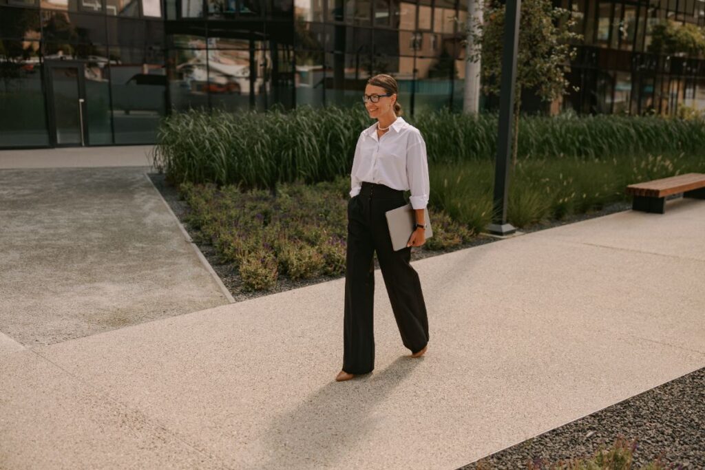 Une femme qui marche dans la rue habillée en chemise blanche, pantalon noir et talon pointu