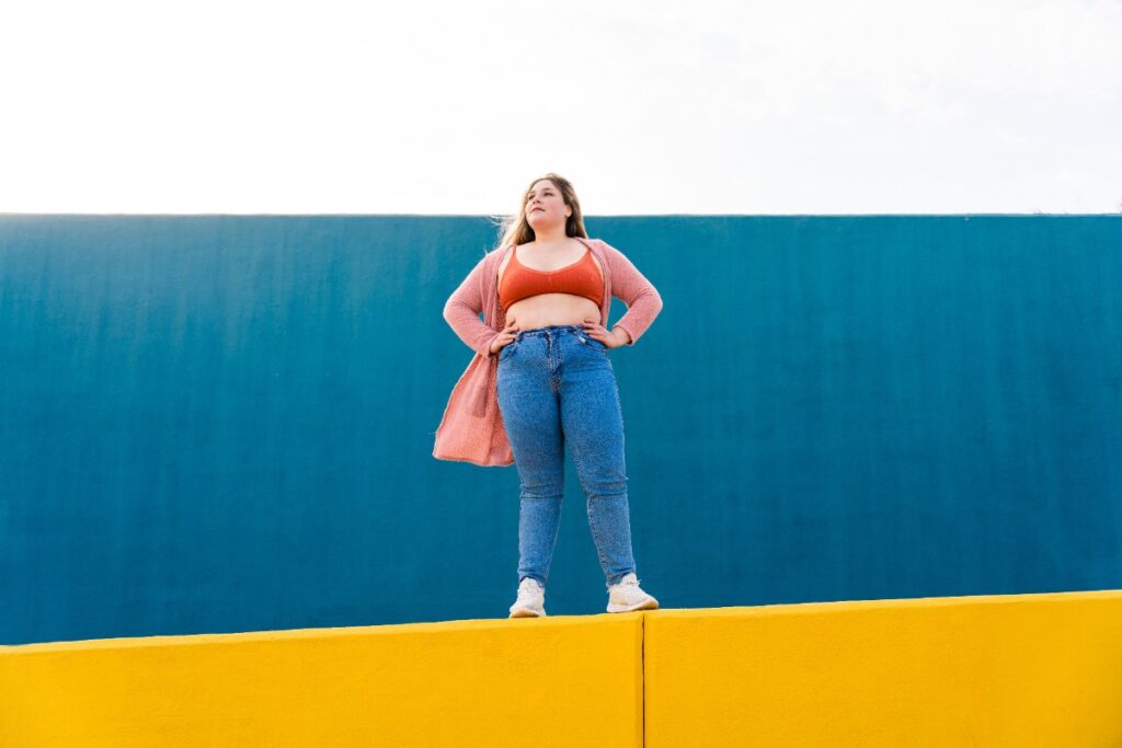 Une femme ronde portant un pantalon jeau bleu et un cardigan rose