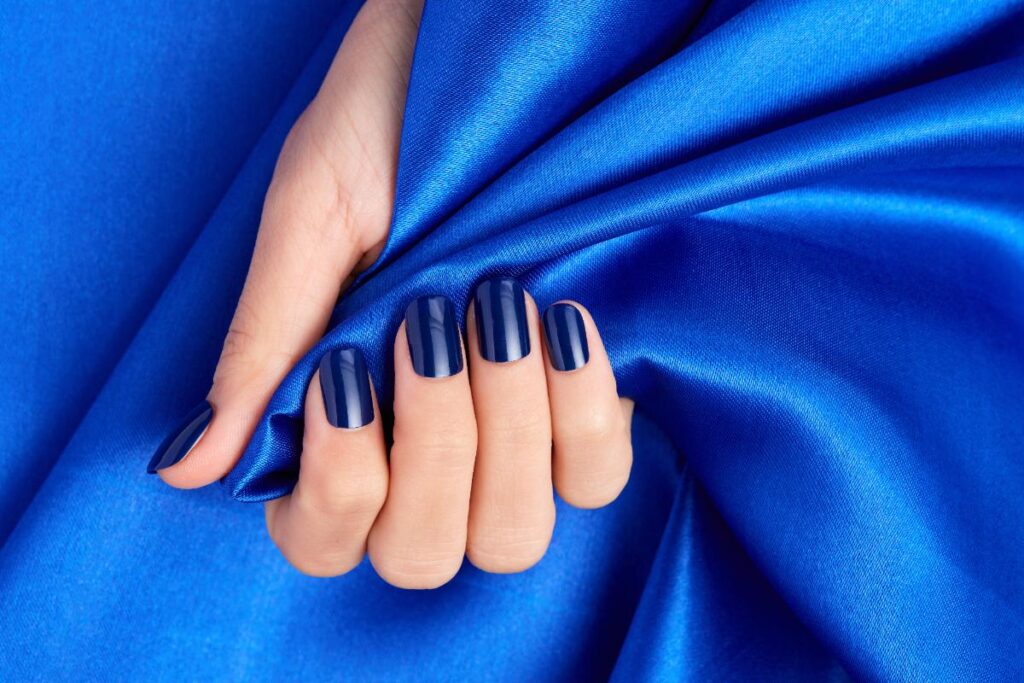 Main avec des ongles manucurés tenant un tissu bleu