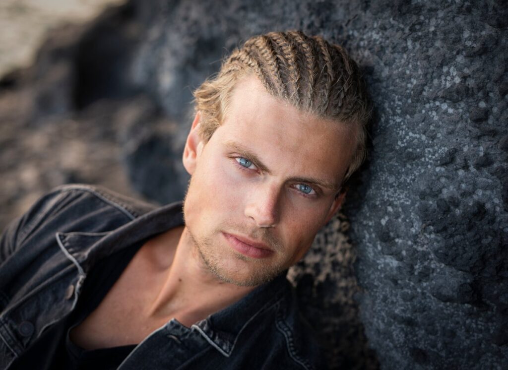 Un bel homme blond avec des tresses appuyé sur le mur