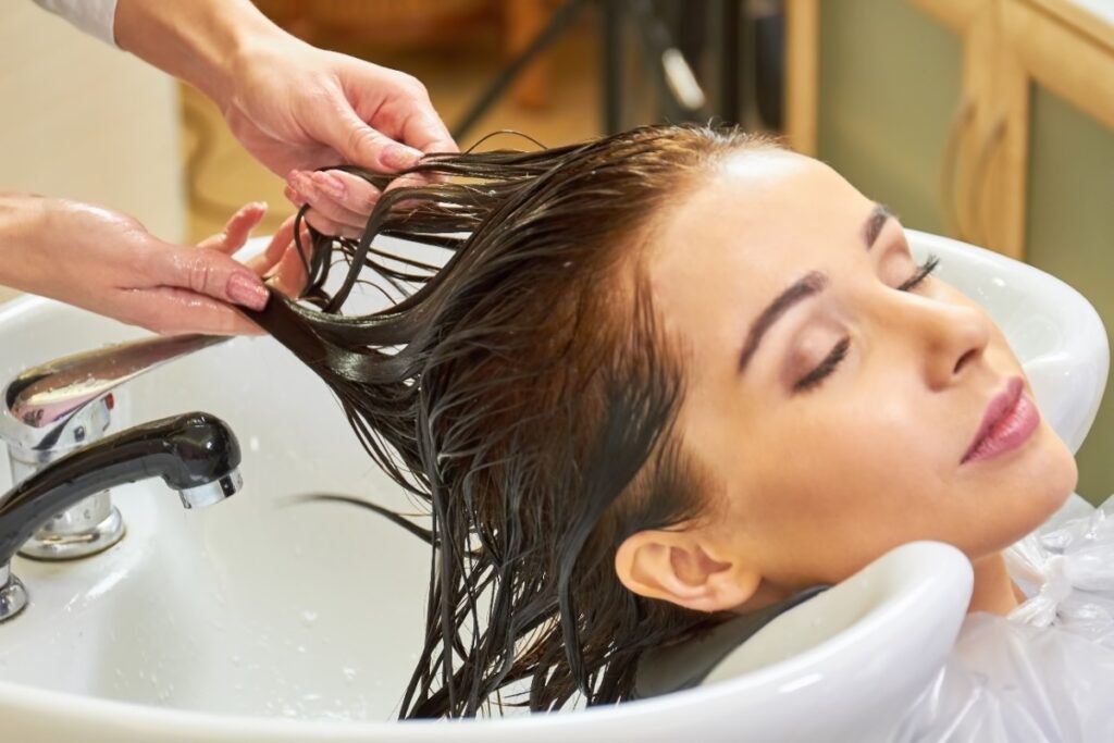 Une femme se relaxant pendant le lavage de son cheveux dans un salon de coiffure