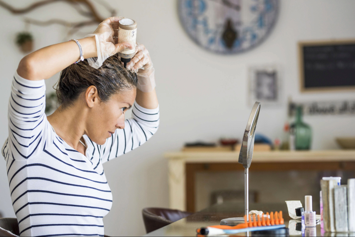 Une femme regarde le mirroir et applique le masque fait maison comme soin de ses cheveux